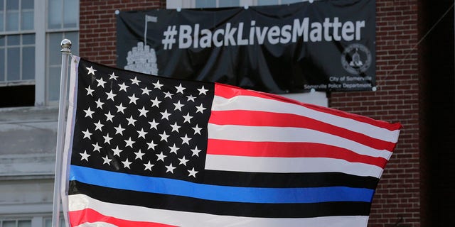 FILE - In this July 28, 2016, file photo, a flag with a blue and black stripes in support of law enforcement officers, flies at a protest by police and their supporters outside Somerville City Hall in Somerville, Mass.   An Oregon county has agreed to pay $100,000 to a black employee who sued after a co-worker pinned up a "Blue Lives Matter" flag. The Oregonian/OregonLive reports Saturday, April 20, 2019, that Karimah Guion-Pledgure alleged in her January lawsuit that the flag demeans the "Black Live Matter" movement. (AP Photo/Charles Krupa, File)