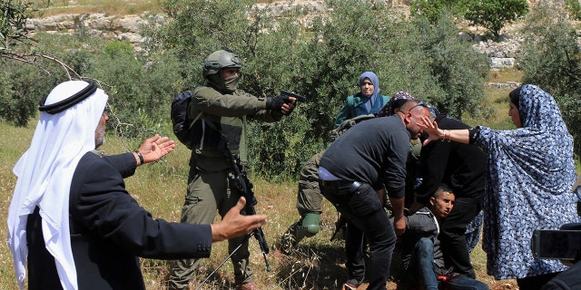 An Israeli soldier points his gun at a group of Palestinians gathering around a wounded Osama Hajahjeh (16) near the village of Tekoa. West Bank. (AP Photo / Mustafa Allbadan)