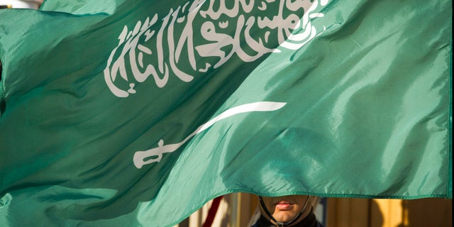 A Saudi Honor Guard member is covered by the flag of Saudi Arabia in 2019