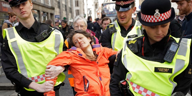 Police remove an Extinction Rebellion climate change protester who blocked a road outside the Goldman Sachs office in the City of London, Thursday, April 25, 2019.