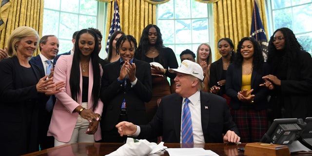 President Donald Trump laughs out loud as he wears a hat that was presented to him while he welcomed the members of the Baylor Women's Basketball Team, who are the national champions of the 2019 NCAA Division 1 at the White House Oval Office in Washington, DC, Monday, April 29, 2019. Baylor Women's Basketball Head Coach Kim Mulkey, left, stares. (AP Photo / Susan Walsh)