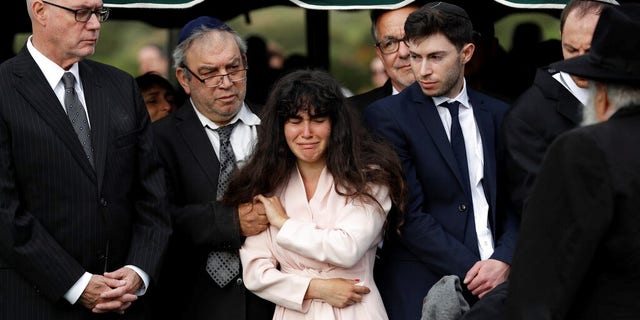 Hannah Kaye, the daughter of shooting victim Lori Kaye, center, holds the hand of her father, Howard Kaye, during funeral services, Monday.
