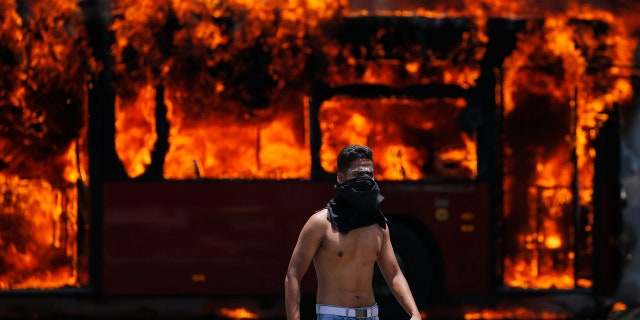 An anti-government protester walks near a bus that was set on fire by opponents of Venezuela's President Nicolas Maduro during clashes between rebel and loyalist soldiers in Caracas, Venezuela, Tuesday, April 30, 2019. Venezuelan opposition leader Juan Guaidó took to the streets with a small contingent of heavily armed troops early Tuesday in a bold and risky call for the military to rise up and oust Maduro. (AP Photo/Fernando Llano)