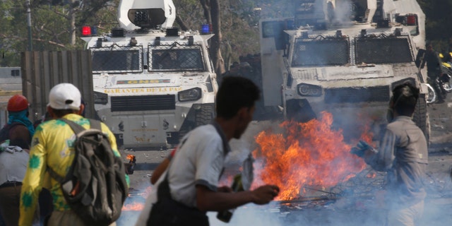 Opponents to Venezuela's President Nicolas Maduro face off with Bolivarian National Guards in armored vehicles who are loyal to the president, during an attempted military uprising in Caracas, Venezuela, Tuesday, April 30, 2019. Opposition leader Juan Guaido took to the streets with a small contingent of heavily armed troops in a call for the military to rise up and oust Maduro. (AP Photo/Ariana Cubillos)