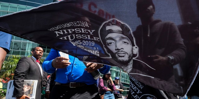 A fan of rapper Nipsey Hussle holds a flag with Hussle's image on it as he attends a public memorial at Staples Center in Los Angeles, Thursday, April 11, 2019. (AP Photo/Ringo H.W. Chiu)