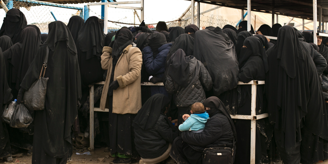 In this Sunday, March 31, 2019 photo, a woman waits with her baby for aid supplies at Al-Hol camp, in Hassakeh province, Syria. An international aid group says it recorded 31 deaths in the final week of March among people making their way out of the last sliver of territory held by the Islamic State group and toward a camp for the displaced. The International Rescue Committee says Monday the highest weekly death rate reflects the desperate conditions of the mostly women and children who left the village of Baghouz for al-Hol camp. The IRC figures could not be independently confirmed. (AP Photo/Maya Alleruzzo)