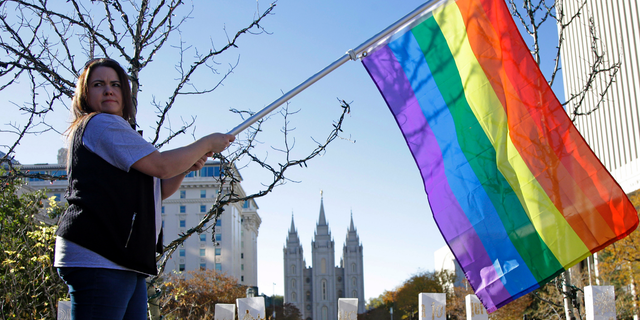 FILE - In this Nov. 14, 2015 file photo, Sandy Newcomb poses for a photograph with a rainbow flag as people gather for a mass resignation from The Church of Jesus Christ of Latter-day Saints in Salt Lake City. The Church of Jesus Christ of Latter-day Saints is repealing rules unveiled in 2015 that banned baptisms for children of gay parents and made gay marriage a sin worthy of expulsion. The surprise announcement Thursday, April 4, 2019, by the faith widely known as the Mormon church reverses rules that triggered widespread condemations from LGBTQ members and their allies. (AP Photo/Rick Bowmer, File)