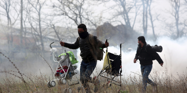 A man holding two baby strollers runs to avoid tear gas thrown by riot police during clashes outside a refugee camp in the village of Diavata, west of Thessaloniki, northern Greece, Friday, April 5, 2019. Clashes broke out Thursday between migrants and Greek police outside a camp in northern Greece, where hundreds gathered in the hope of reviving a route that saw hundreds of thousands enter more prosperous countries in Europe. (AP Photo/Giannis Papanikos)