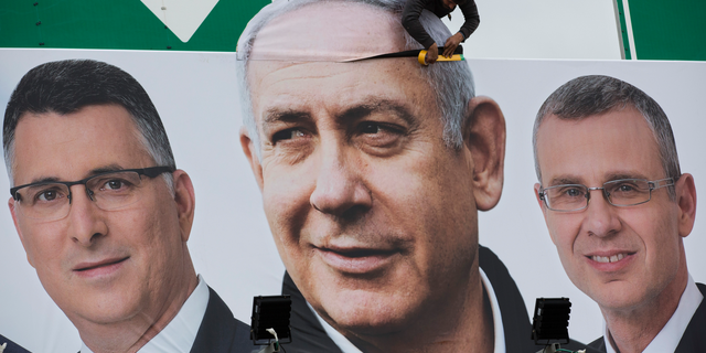 A man works on a Likud party election campaign billboard depicting Israeli Prime Minister Benjamin Netanyahu, center, and his party candidates, in Petah Tikva, Israel, Monday, April 1, 2019. (AP Photo/Oded Balilty)