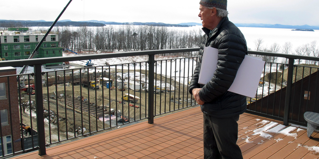 In this March 7, 2019 photo, developer Eric Farrell looks at construction on the property that once housed Burlington College, and before that was an orphanage run by the Roman Catholic Diocese, on the shore of ice-covered Lake Champlain, background, in Burlington, Vt. The property is being redeveloped and city officials say it will be a boost to the entire community. (AP Photo/Wilson Ring)