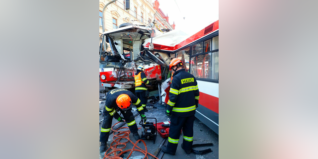 In this handout photo taken on Monday April 1, 2019, firemen stand by a tram that has collided with trolleybus in Brno, Czech Republic. Officials say a tram collided with a trolleybus head on in the Czech second largest city, injuring dozens of passengers. Michaela Bothova, a spokeswoman for the rescue service says at least five people have suffered serious injuries while another 20 passengers were injured lightly. (HZS JMK via AP)
