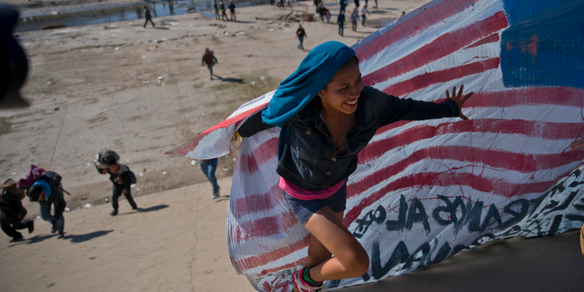 In this Nov. 25, 2018 file photo, a migrant woman helps carry a handmade U.S. flag up the riverbank at the Mexico-U.S. border after getting past Mexican police at the Chaparral border crossing in Tijuana, Mexico.