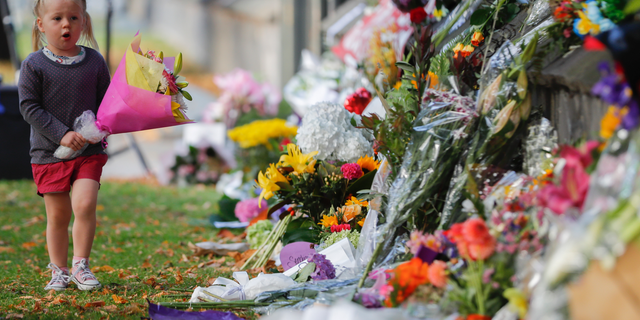 FILE - In this March 17, 2019, file photo, a girl carries flowers to a memorial wall following the mosque shootings in Christchurch, New Zealand. New Zealand's parliament on Wednesday passed sweeping gun laws which outlaw military-style weapons, less than a month after the nation's worst mass shooting left 50 dead and 39 wounded in two mosques in the South Island city of Christchurch. (AP Photo/Vincent Thian, File)