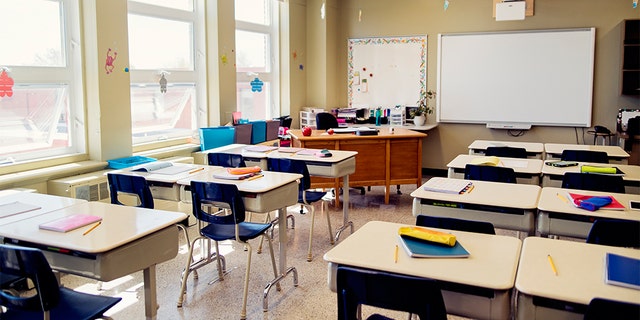 Empty elementary classroom during recess. Interactive whiteboard at the side of teacher’s desk. 