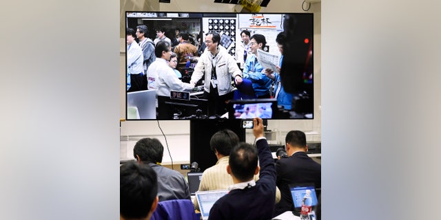 Members of the Japan Aerospace Exploration Agency, or JAXA, seen on the screen, celebrate the event as the Hayabusa2 space shuttle was safely evacuated and remained intact after the blast, to Sagamihara, near Tokyo, on Friday, April 5, 2019.