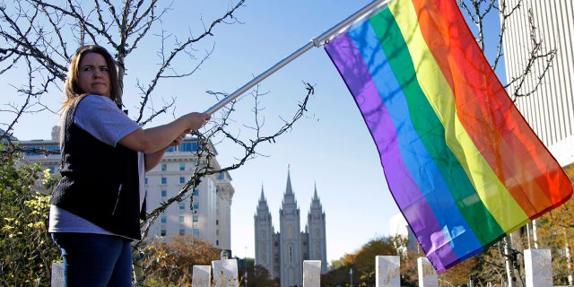 Sandy Newcomb poses for a photograph with a rainbow flag in front of The Church of Jesus Christ of Latter-day Saints in Salt Lake City.