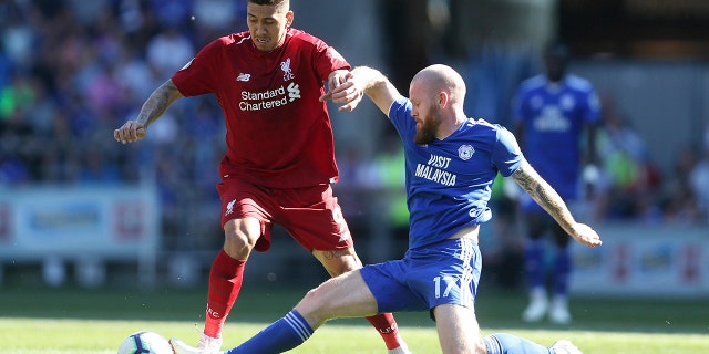 Liverpool's Roberto Firmino, left, and Cardiff City's Aron Gunnarsson battle for the ball during the English Premier League soccer match at The Cardiff City Stadium, Cardiff, Wales, Sunday April 21, 2019. (David Davies/PA via AP)
