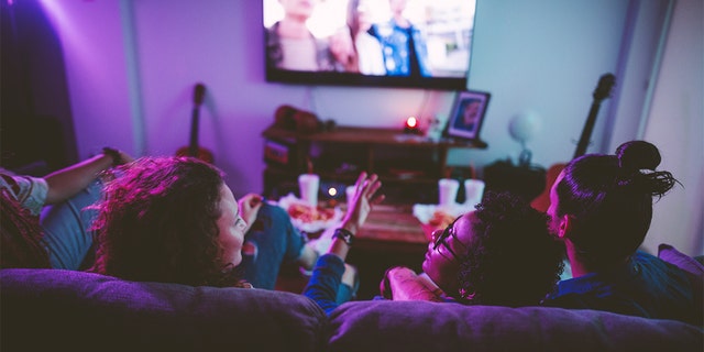 Friends relaxing on living room sofa and watching film on TV