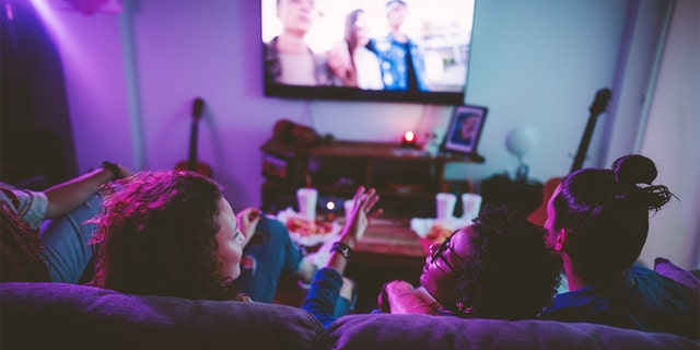 Friends relaxing on sofa in living room and watching movie on tv