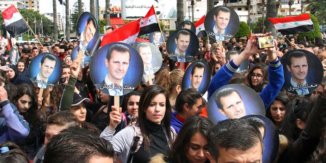 In this photo released by the Syrian official news agency SANA, people hold Syrian flags and portraits of President Bashar Assad during a protest against U.S. President Donald Trump's move to recognize Israeli sovereignty over the Israeli occupied Golan Heights, in the coastal port city of Tartus, Syria, Wednesday, March. 27, 2019.