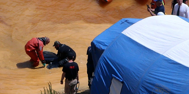 A travel suitcase containing the decomposing remains of an adult woman and a concrete block was retrieved from the bottom of a man-made lake, officials said Sunday.