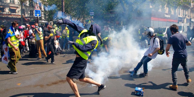 A demonstrator throws back a tear gas canister during a Yellow Vest demonstration in Paris, Saturday, April 20, 2019. 