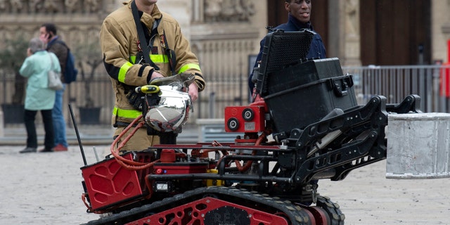 Firefighters are seen with a robot firefighter called Colossus, made by French robotics company Shark Robotics, outside Notre-Dame Cathedral after a major fire on April 16, 2019.