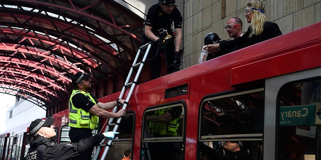 Police remove climate activists who glued themselves on top of a Dockland Light Railway train at Canary Wharf station in east London as part of the ongoing climate change protests.