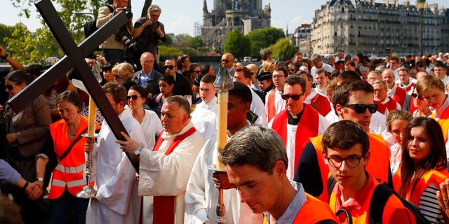 With Notre Dame cathedral in background, religious officials carry the cross during the Good Friday procession, Friday, April 19, 2019 in Paris.