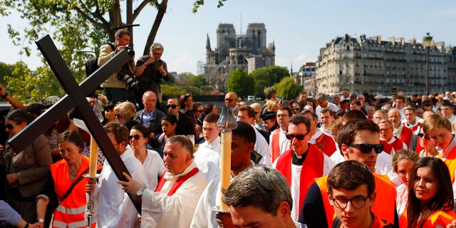 With Notre Dame cathedral in background, religious officials carry the cross during the Good Friday procession, Friday, April 19, 2019 in Paris.