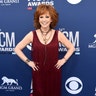 Reba McEntire hits the carpet in a burgundy dress with fringe detailing before she takes the 2019 ACM Awards stage to host one of country music's biggest nights.