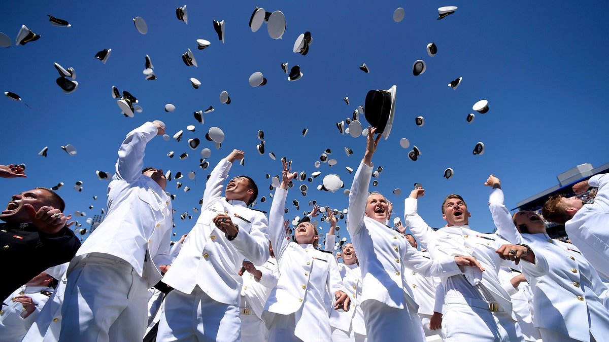 Naval Academy graduates wearing white uniforms celebrate by throwing their hats in the air