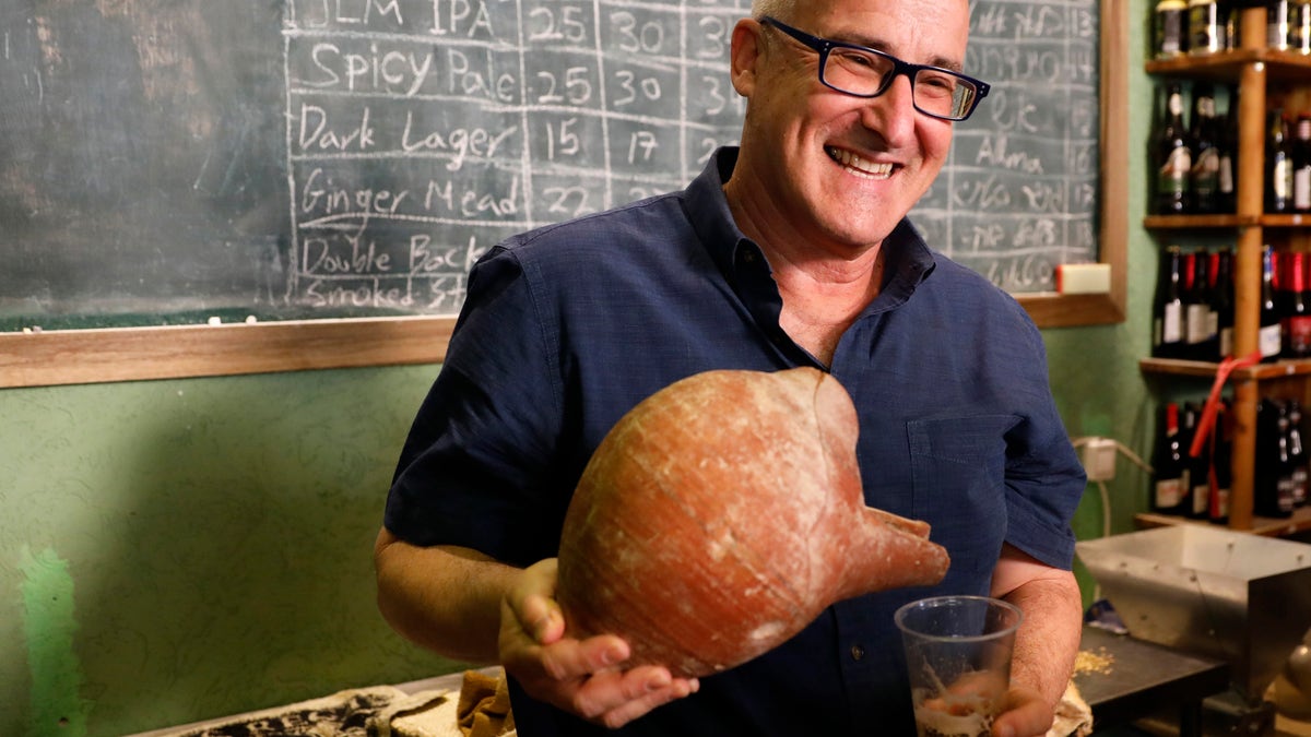 Prof. Aren Maeir, from Bar Ilan University, holds an ancient jar and a glass of beer during a press conference in Jerusalem, Wednesday, May 22, 2019. (AP Photo/Sebastian Scheiner)