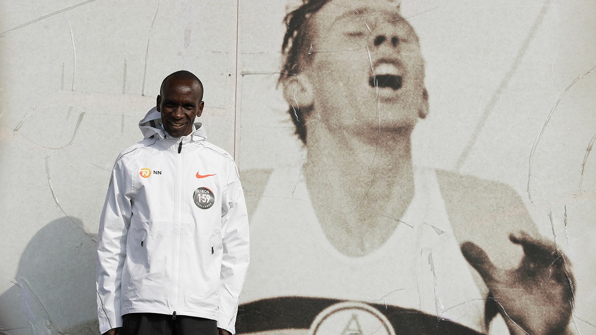 Marathon world record holder Kenya's Eliud Kipchoge poses for photographers next to an image of British athlete Roger Bannister, who in 1954 ran to become the first person ever to break the four-minute mile barrier, at the Iffley Road Track, in Oxford, England, Tuesday, April 30, 2019. (AP Photo/Matt Dunham)