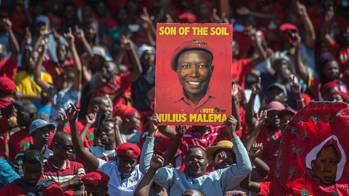 Supporters of the Economic Freedom Fighters (EFF) party, hold up an election poster of leader Julius Malema during a May Day Rally in Alexandra Township, Johannesburg, Wednesday, May 1, 2019. (AP Photo/Mujahid Safodien)