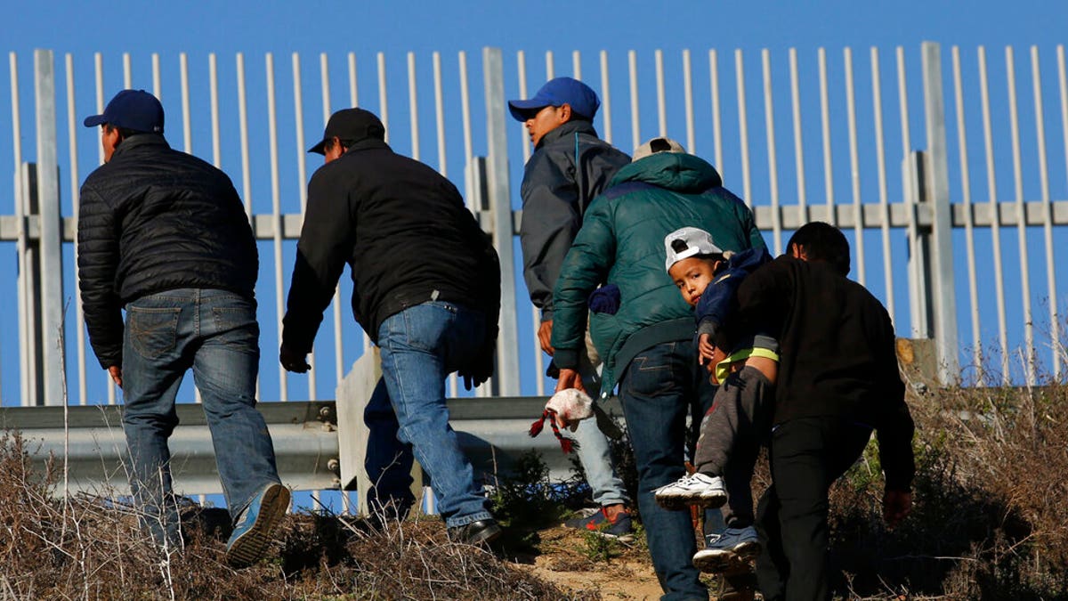 FILE: Honduran migrants, one carrying a child, who plan to turn themselves over to U.S. border patrol agents, walk up the embankment after climbing over the U.S. border wall from Tijuana, Mexico. 