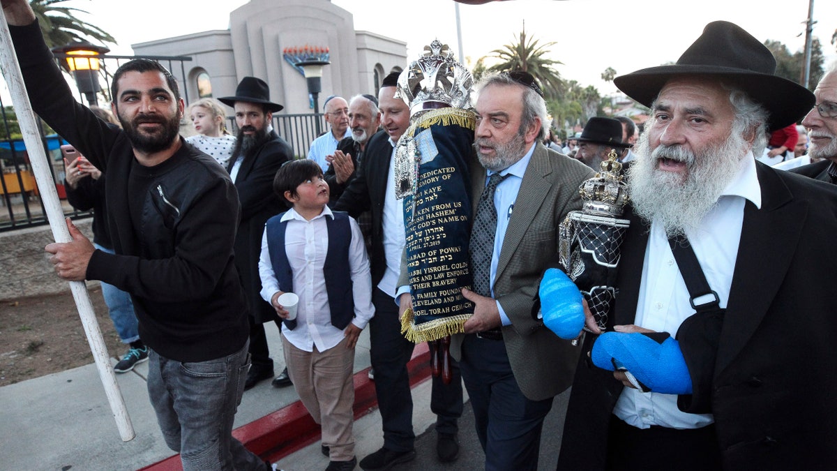 Howard Kaye, center, husband of Lori Kaye, carries the new Torah as Rabbi Yisroel Goldstein, right, and other members of the Chabad of Poway synagogue celebrate the completion of the new scroll dedicated to Lori Kaye, who was killed when a gunman attacked the synagogue in April on Wednesday, May 22, 2019, in Poway, Calif. (Hayne Palmour IV/The San Diego Union-Tribune via AP)