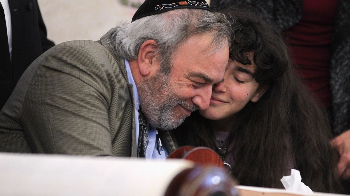 Howard Kaye, center, and his daughter Hannah Kaye, hug after the final letter was inked into the new Torah that's dedicated to wife and mother Lori Kaye, who was killed when a gunman attacked the Chabad of Poway in April, during a celebration for the new scroll at the synagogue, Wednesday, May 22, 2019, in Poway, Calif. (Hayne Palmour IV/The San Diego Union-Tribune via AP)