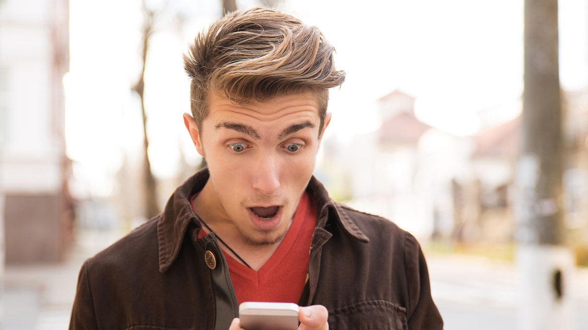 Young shocked man receiving news on smartphone and looking shocked while standing on street