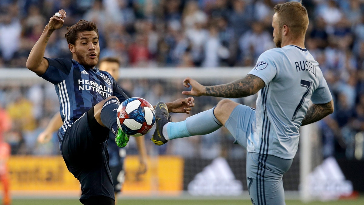 Sporting Kansas City forward Johnny Russell (7) and LA Galaxy midfielder Jonathan dos Santos compete for the ball during the first half of an MLS soccer match Wednesday, May 29, 2019, in Kansas City, Kan. (AP Photo/Charlie Riedel)