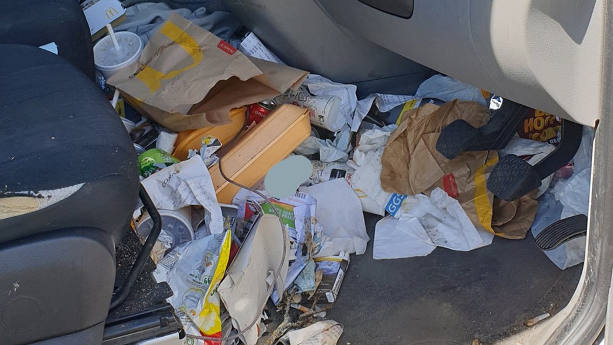 In the image, McDonald’s wrappers and cups, Styrofoam containers, receipts, documents and various other indiscernible pieces of garbage can be seen spilling out of the driver’s side cab, on the dash and behind the driver pedals.