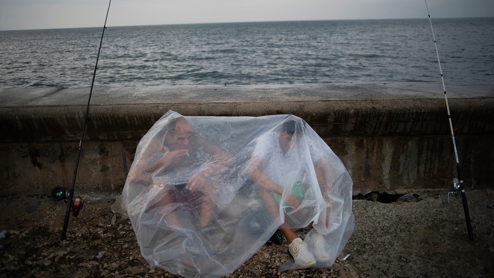 Engelbert Canete, and Ethian Jesus, protect themselves from the rain with a plastic sheet while fishing at the Malecon in Havana, Cuba, May 6, 2019. 