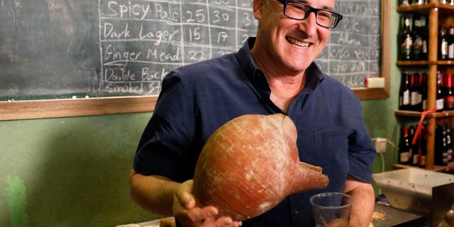 Prof. Aren Maeir, from Bar Ilan University, holds an ancient jar and a glass of beer during a press conference in Jerusalem, Wednesday, May 22, 2019. (AP Photo/Sebastian Scheiner)