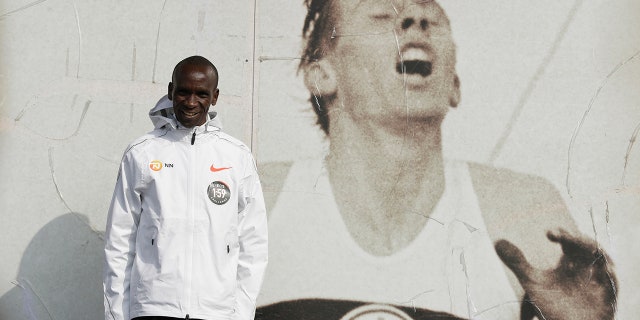 Marathon world record holder Kenya's Eliud Kipchoge poses for photographers next to an image of British athlete Roger Bannister, who in 1954 ran to become the first person ever to break the four-minute mile barrier, at the Iffley Road Track, in Oxford, England, Tuesday, April 30, 2019. (AP Photo/Matt Dunham)