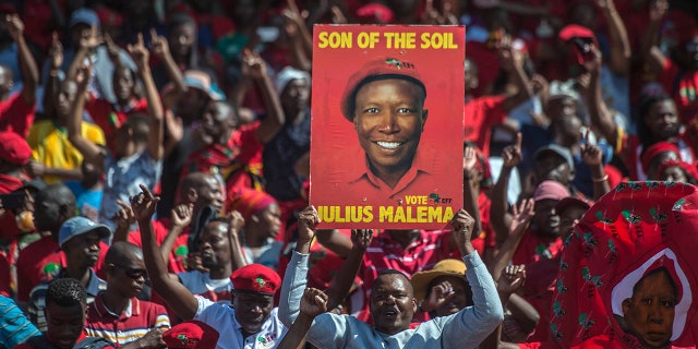Supporters of the Economic Freedom Fighters (EFF) party, hold up an election poster of leader Julius Malema during a May Day Rally in Alexandra Township, Johannesburg, Wednesday, May 1, 2019. (AP Photo/Mujahid Safodien)