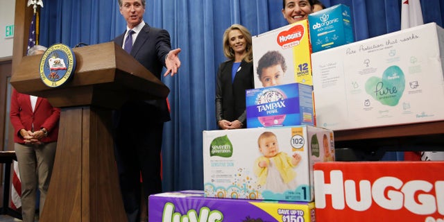 Gov. Gavin Newsom gestures towards boxes of tampons and diapers after proposing to eliminate from the state sales tax on such products in his upcoming state budget during a news conference. (Associated Press)