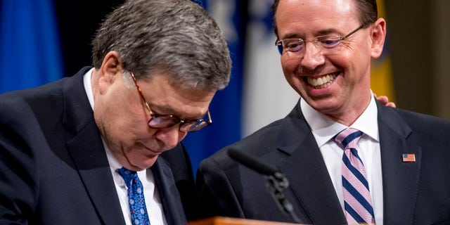 Attorney General William Barr, left, pausing as he brings Deputy Attorney General Rod Rosenstein, to the podium to ask who has the more stoic face during a farewell ceremony for Rosenstein in the Great Hall at the Department of Justice in Washington last week. (AP Photo/Andrew Harnik)
