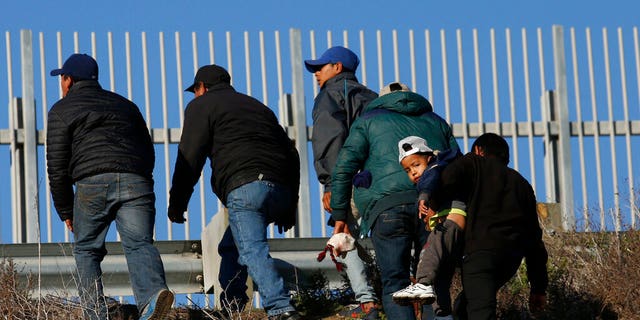 FILE: Honduran migrants, including one who is carrying a child and planning to surrender to US Border Patrol agents, make their way up the embankment after crossing the US border wall in Tijuana, Mexico. 