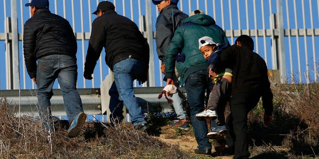 FILE: Honduran migrants, one carrying a child, who plan to turn themselves over to U.S. border patrol agents, walk up the embankment after climbing over the U.S. border wall from Tijuana, Mexico.