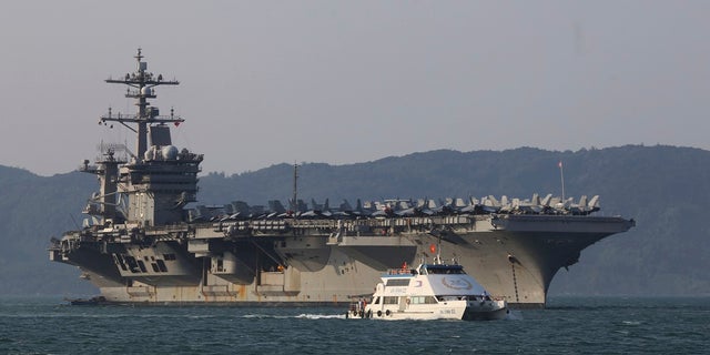 In this March 5, 2018, file photo, a Vietnamese passenger boat sails past U.S. aircraft carrier USS Carl Vinson as it docks in Danang bay, Vietnam. A U.S. sailor has pleaded guilty to espionage and sentenced to three years after admitting he took classified information about a Navy's nuclear-powered warship and planned to give it to a journalist and then defect to Russia officials said Friday, (AP Photo/Hau Dinh, File)